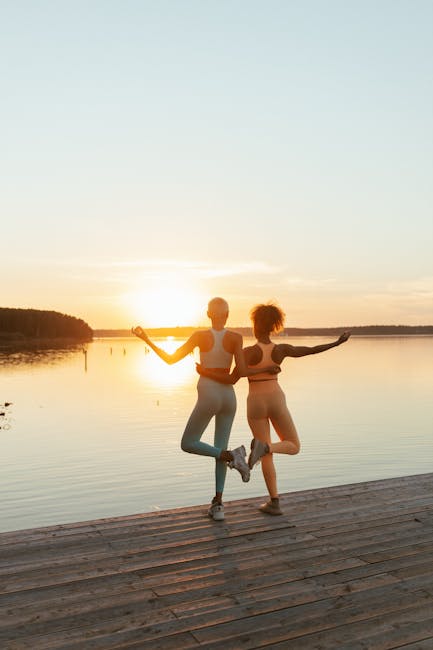 Woman practicing yoga on a wooden dock by a calm lake at sunrise.